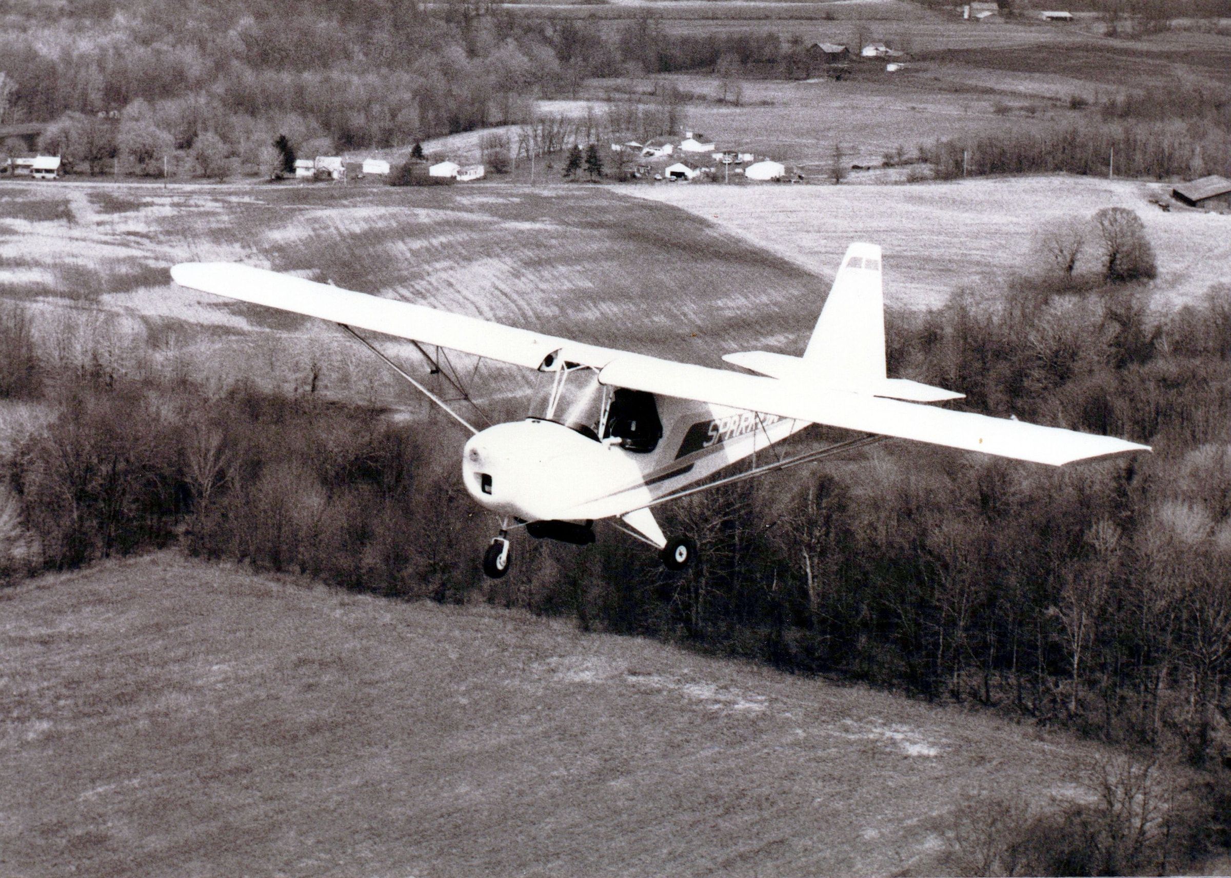 Black-and-white photograph of an early Carlson Sparrow in flight over farmland