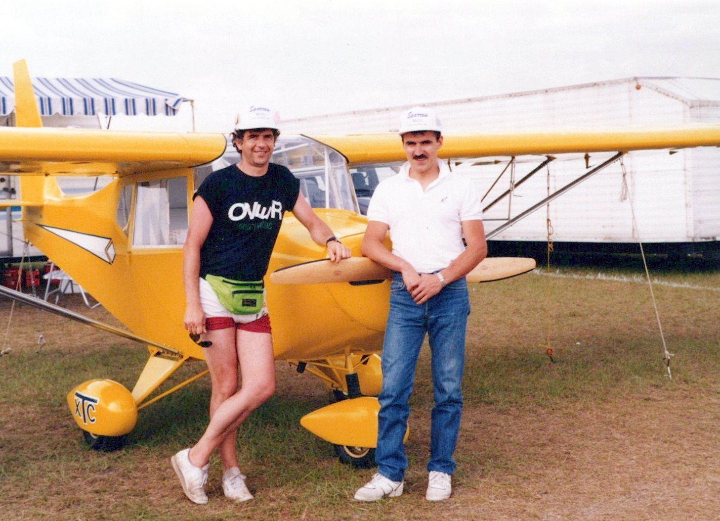 Two visitors standing beside the yellow Carlson Sparrow II XTC, showing its XTC wheel pants