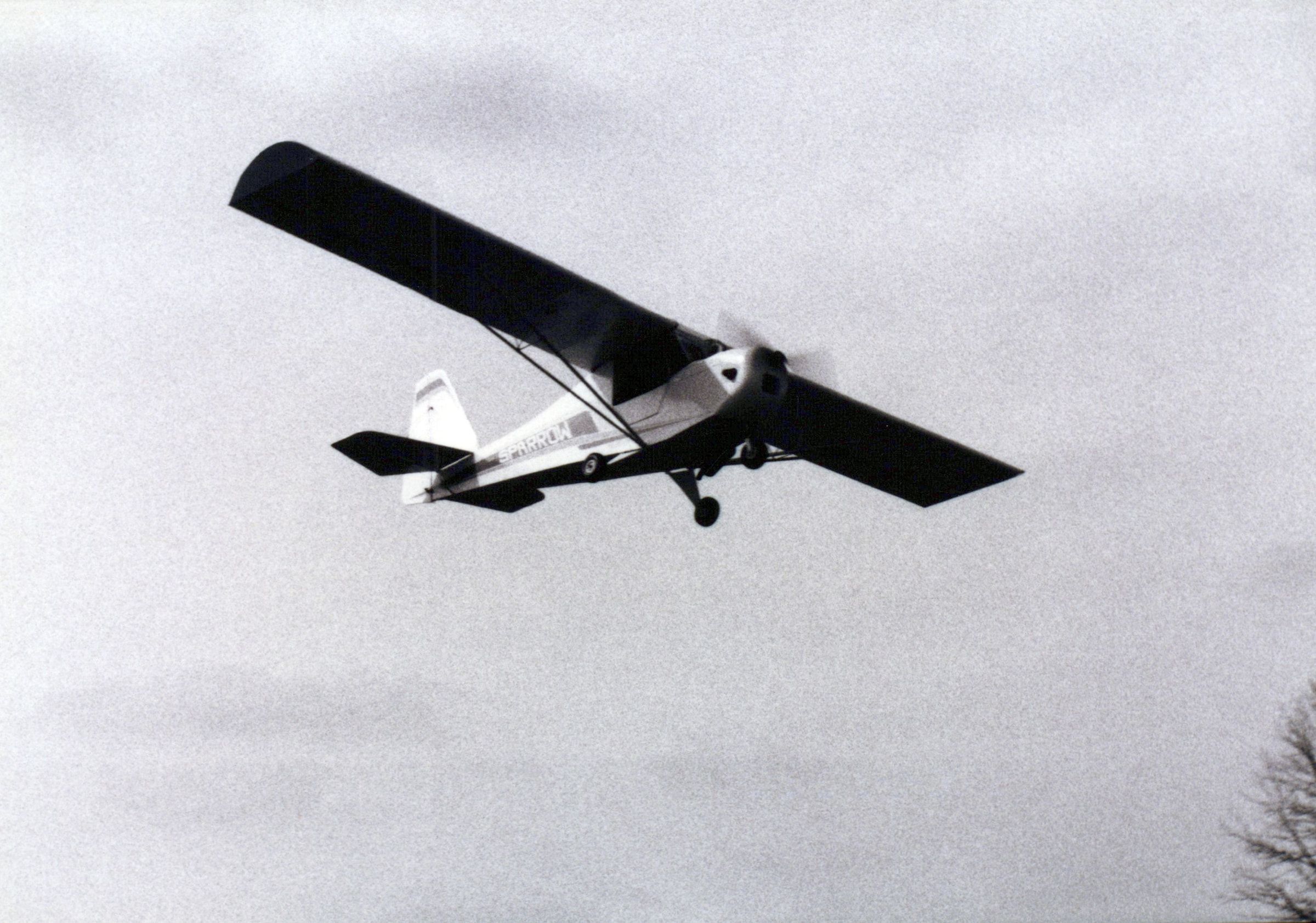 Black-and-white photograph of a Carlson Sparrow Ultralight banking overhead