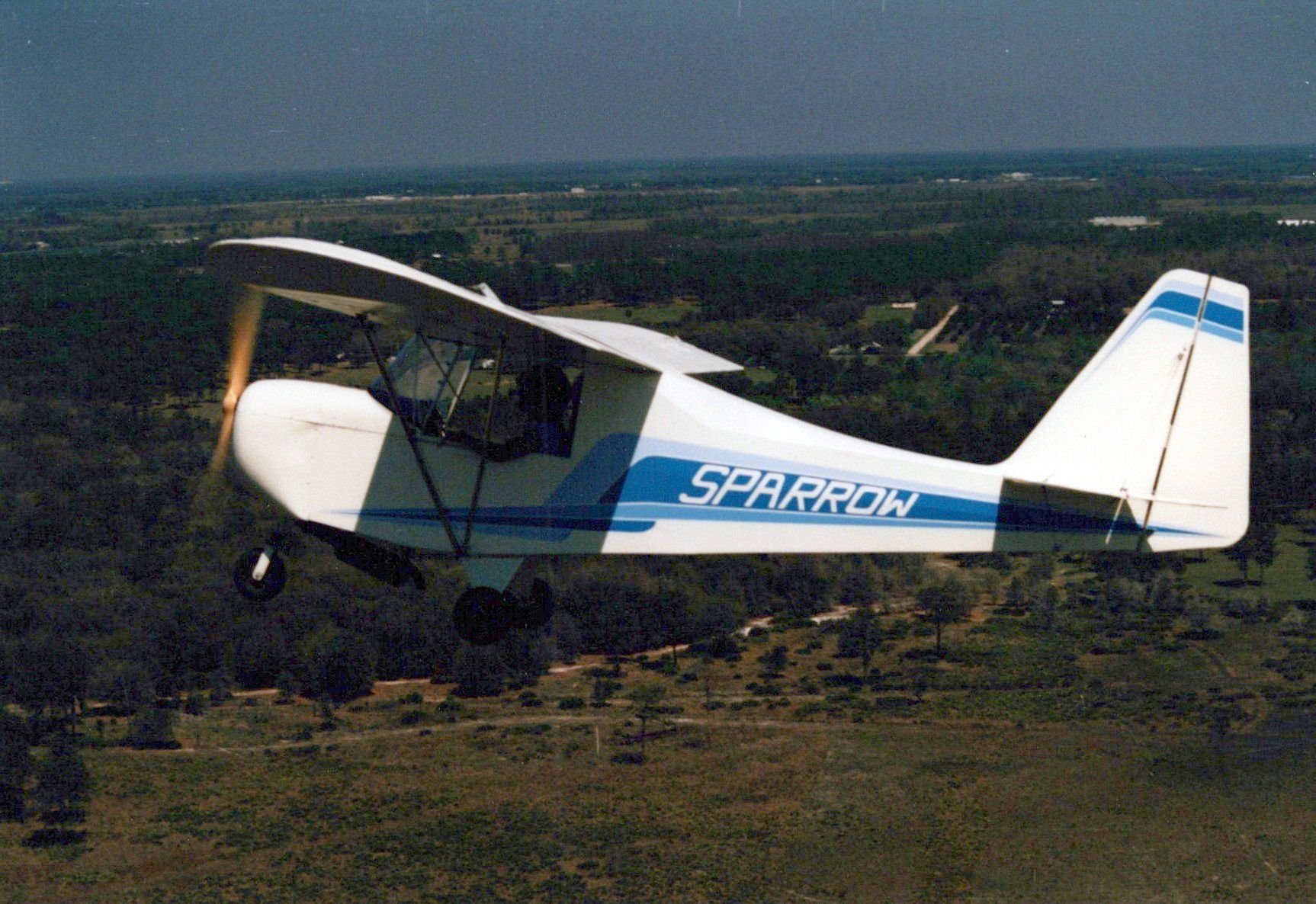 White and blue Carlson Sparrow Ultralight in flight, seen from the side