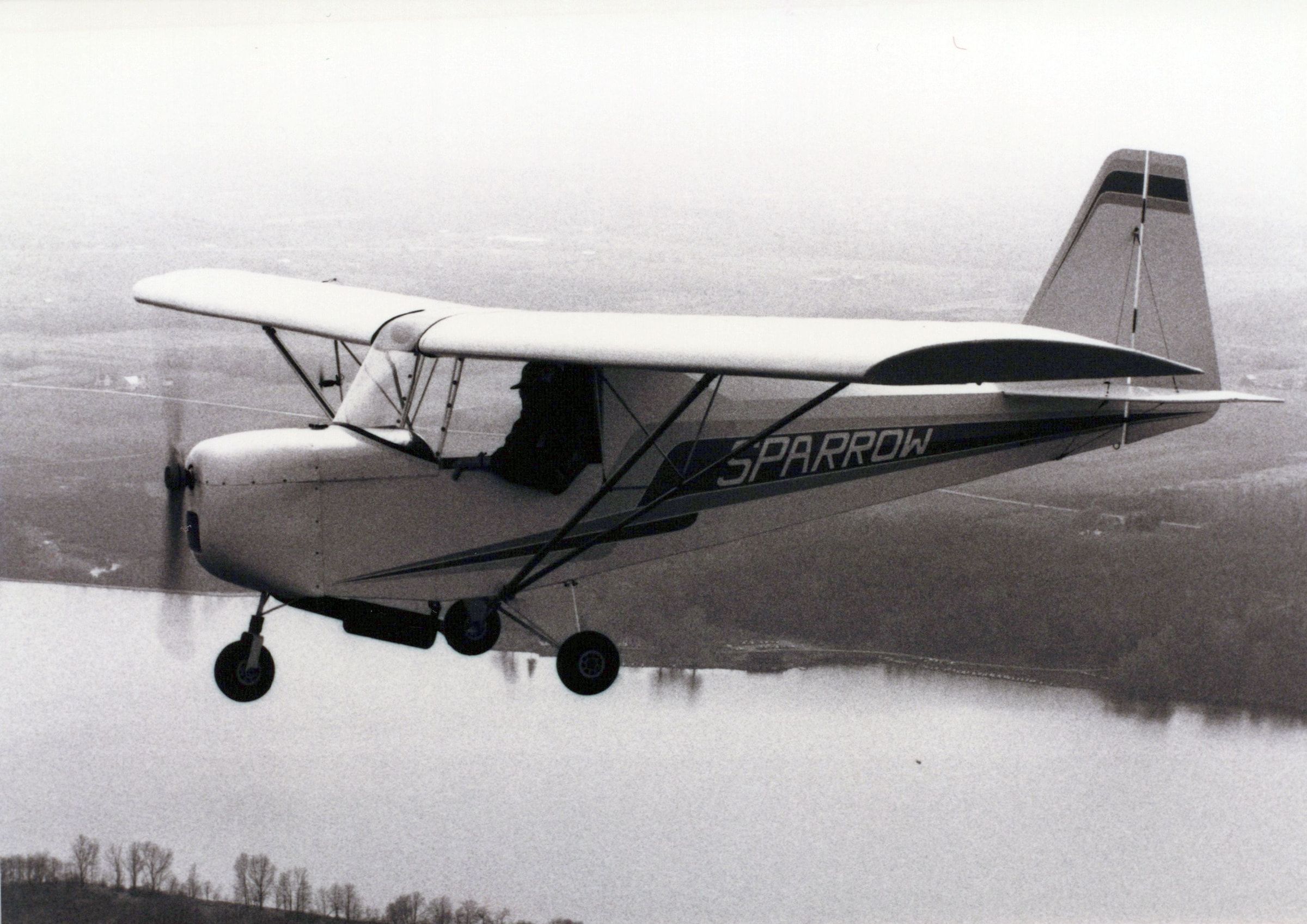 Black-and-white photograph of a Carlson Sparrow Ultralight flying over water