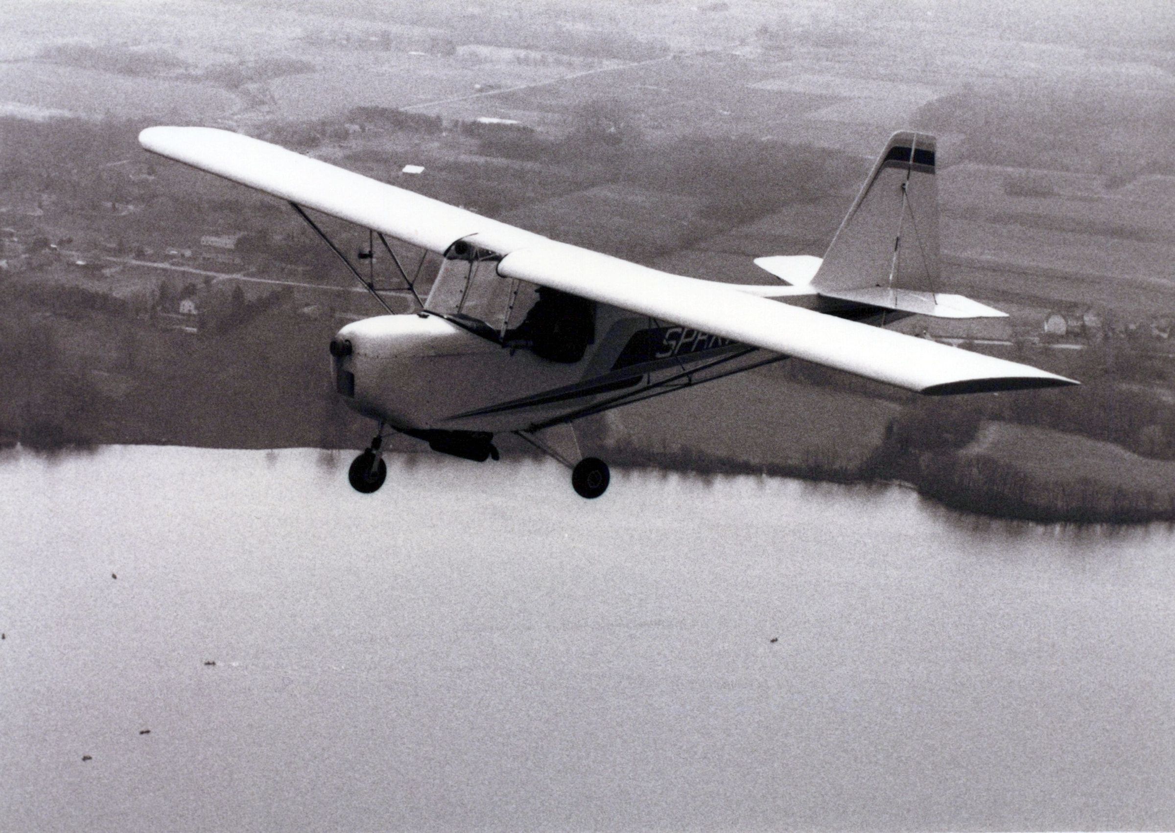 Black-and-white photograph of a Carlson Sparrow Ultralight flying over a lake