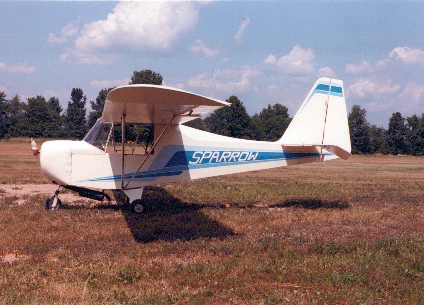 White and blue Carlson Sparrow Ultralight parked on a dry grass field